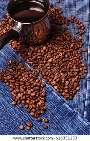 Old cezve and black coffee beans on jeans background