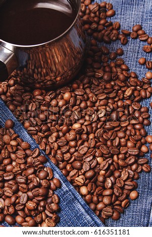 Old cezve and black coffee beans on jeans background