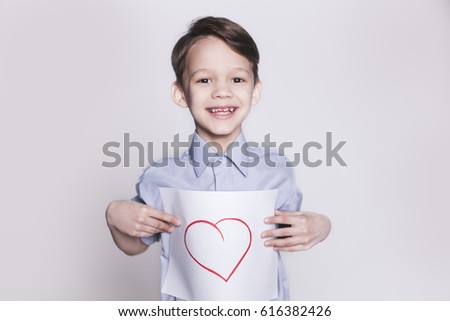 Portrait of young happy smiling brunette boy with picture of heart on the sheet of paper in hands looking at camera isolated.