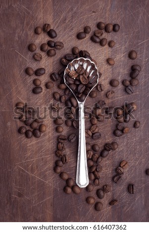 Spoon with coffee beans over wooden background.