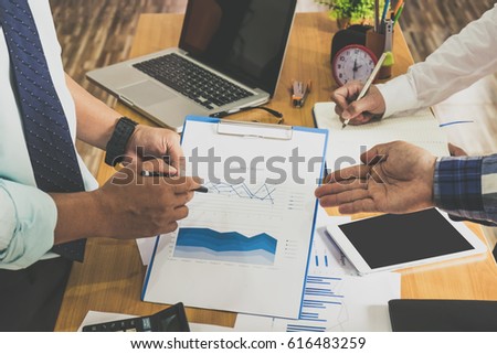 Business people brainstorming at office desk, they are analyzing financial reports and pointing out financial data on a sheet

