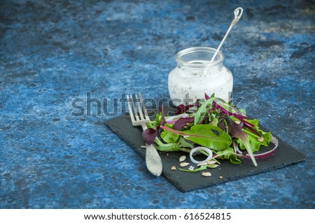 Spring herbs red onion pumpkin flax sesame seeds salad with spicy sour cream sauce served on a black stone board on a blue background