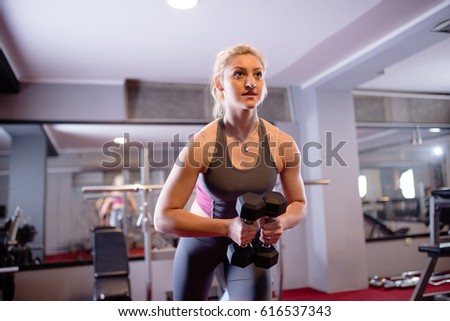 Beautiful young woman exercising with weights in gym
