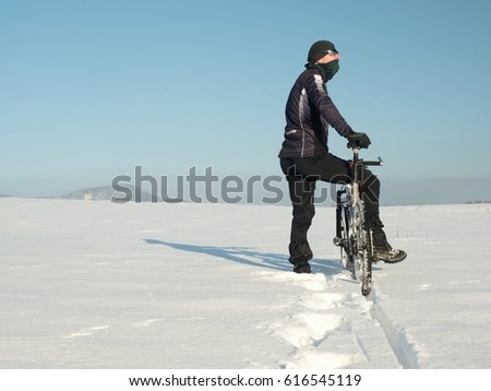 Biker pushing mountain bike on snow drift. Freeze sunny winter weather. Biker is pushing bike in deep snow in meadow. Amazing sunny day. Small snow flakes in the air
