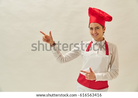 Beautiful woman chef holding out hand in presentation and showing display gesture on empty copy space. Profession and industry job concept. Smiling female chef or baker pointing up empty copy space
