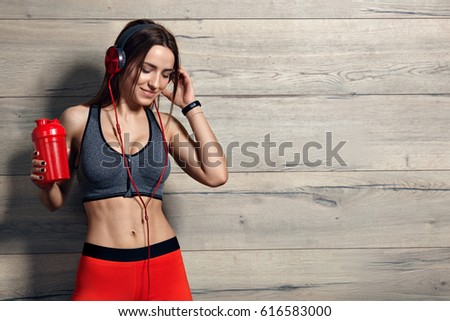 Young beautiful girl listening  music with headphones in the gym. Fitness concept background. Royalty-Free Stock Photo #616583000