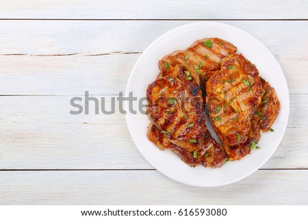 Perfectly seasoned, juicy, delicious grilled pork chops with strips  sprinkled with fresh coriander served on white plate,  on white wooden boards, view from above Royalty-Free Stock Photo #616593080