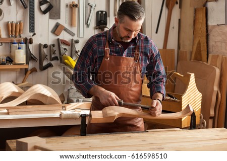 Carpenter works with a planer in a workshop for the production of vintage furniture. He makes cabriole leg for a table in the style of Queen Anne/Joiner Makes Cabriole Leg for Vintage Table Royalty-Free Stock Photo #616598510