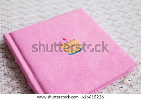 Beautiful photobook in light pink textile cover. Baby photobook with decorative embroidery of birthday cake.   Low depth of sharpness