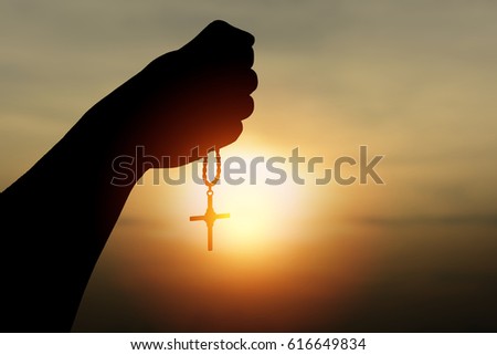 Silhouette rosary against cross in hand. Background sunrise