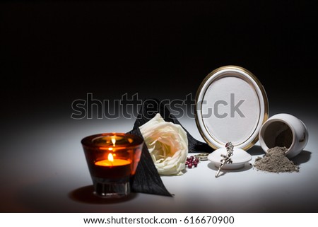 white urn with blank mourning frame, white rose, black tape, candle and rosary for sympathy card on dark background