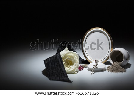 white urn with blank mourning frame, white rose, black tape, and rosary for sympathy card on dark background