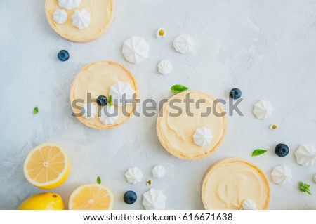 Individual lemon curd tarts with blueberry jam meringue and basil leaves on a white stone background. Flat lay and copy space.