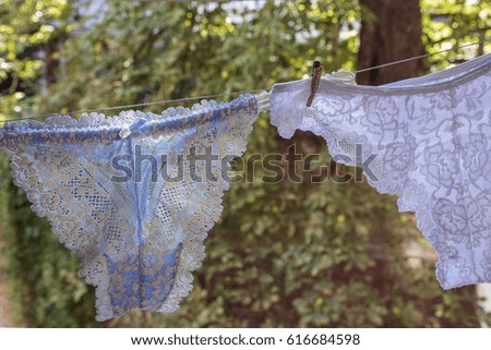 White and blue woman's thongs are drying on the rope in the summer in the day with green leaves as background