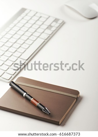 Notepad and pen next to keyboard and mouse on white background.