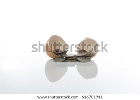 Coins spreading out of a split egg shell over white background