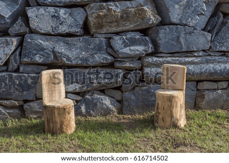 Two handmade wood stools on the garden lawn with different natural stones wall as background