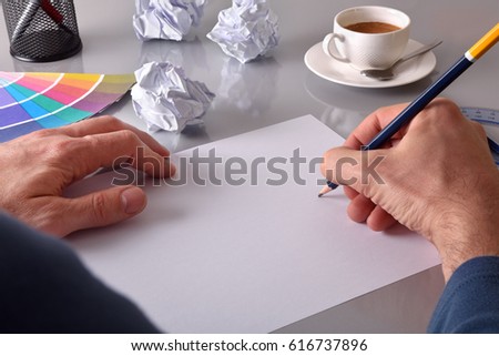 Worker developing an idea on his workbench. Concept search for ideas in business. Blank sheet on gray office table with crumpled sheets and coffee in the background. Elevated view.