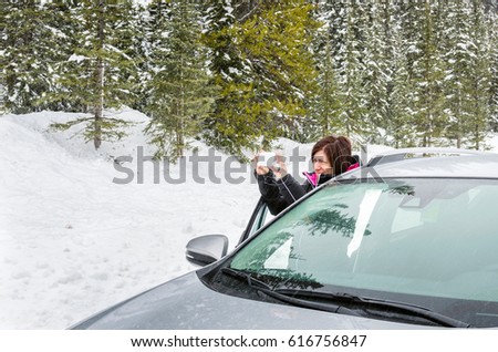 Woman tourist outside her car taking Pictures on a Mountain Road During a Snowstorm
