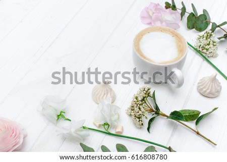 Spring flowers and fragrant delicious boiled black coffee in a white cup and ranunkulyus roses, daffodils and some cookies on wooden background. Good morning concept. Selective soft focus.