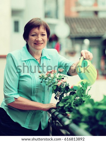 mature woman with watering-can taking care of plants at balcony 