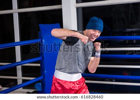 Athletic young male boxer standing in a pose clenching his fists in a boxing ring surrounded by ropes in a gym