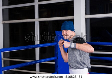 Athletic male boxer standing in a pose clenching his fists in a regular boxing ring surrounded by ropes in a gym