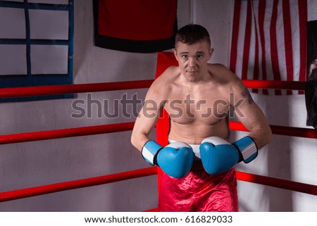 Male boxer with bare chest in boxing gloves standing in a regular boxing ring in a gym