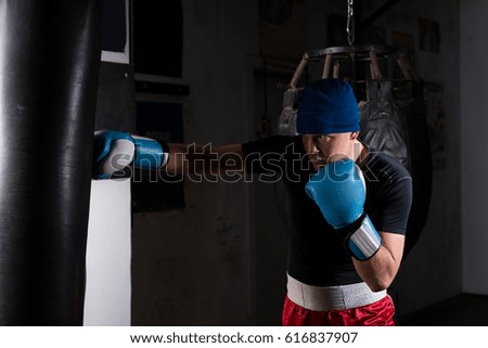 Young man in boxing gloves training with boxing punching bag in a gym