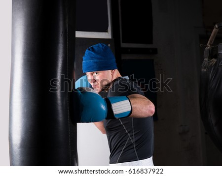Adult sporty boxer in boxing gloves training with boxing punching bag in a gym