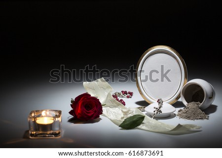 white urn with blank mourning frame, flower,candle, white tape and rosary for sympathy card on dark background