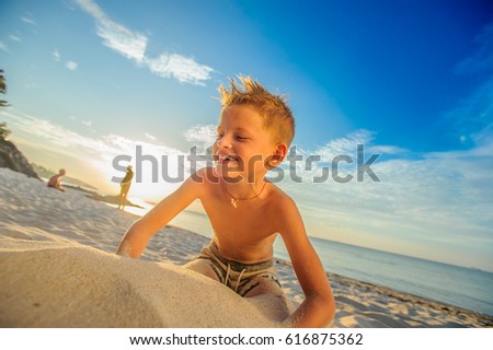 Handsome smiling eight years boy on the tropical beach playing with a stream of sand