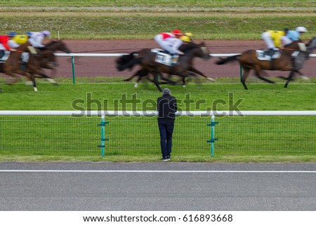 Horse racing. The man at the racetrack looks at the galloping horses. A picture of a man without a face standing with his back. Animals in motion