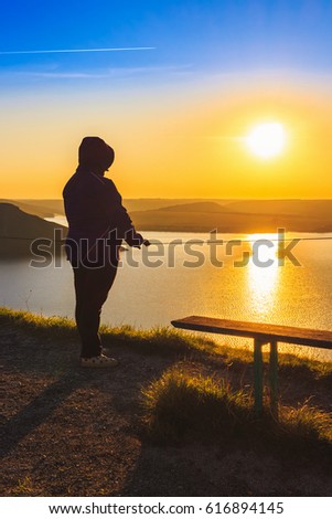 Back view of woman who looks on magnificent sunset on the Dniester river, sun reflected in water