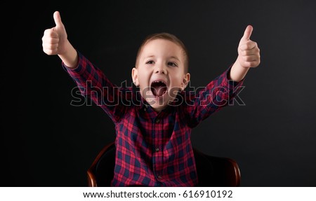 Close-up Portrait of happy boy with a fallen tooth showing thumbs up gesture, isolated over black background. Human emotion, facial expression.
