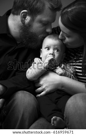 Baby sucking thumb while being kissed by loving parents. Classical black and white family photo with 4-month-old baby boy.