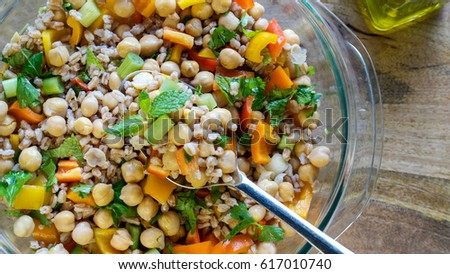 A salad consisting of farro, garbanzo beans, bell peppers, and spring onions served with olive oil on wooden table- healthy vegan eating concept Royalty-Free Stock Photo #617010740