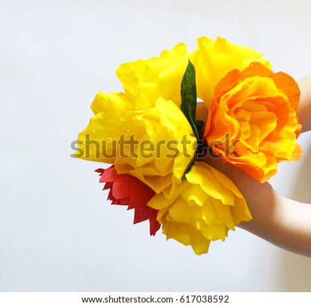 Bouquet of paper flowers in his hands. The child's hands. Handmade. White background. Color yellow, green, orange.