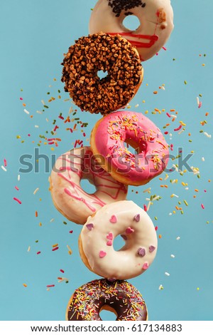 Various decorated doughnuts in motion falling on blue background. Sweet and colourful doughnuts falling or flying in motion. Royalty-Free Stock Photo #617134883