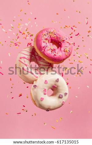 Various decorated doughnuts in motion falling on pink background. Sweet and colourful doughnuts falling or flying in motion.
