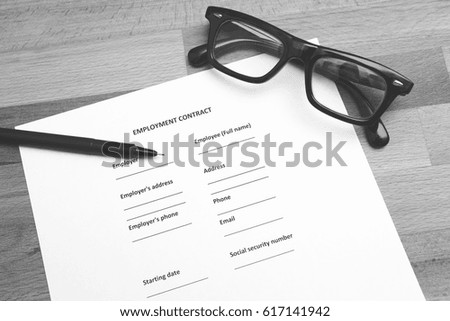 Employment contract to be signed. A pen and glasses on the blank agreement. Wooden table. Image in black and white.