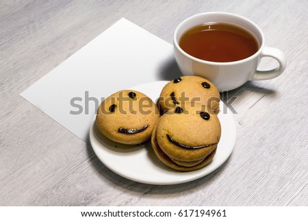 Smile cookies on a white plate with a cup of tea and white paper. Sweet biscuit. Tasty food