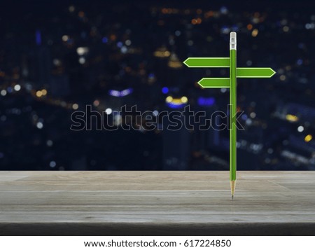 Green pencil with blank sign plate on wooden table over blur colorful night light city tower, Business presentation concept