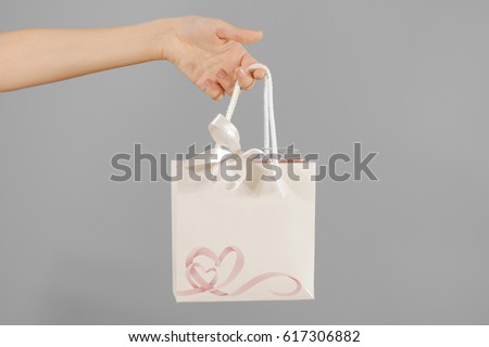 Blank white paper gift bag with hearts mock up holding in hand. Empty plastic package mockup hold in hands isolated. Consumer pack ready for logo design or identity presentation. Product packet handle