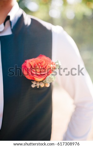 groom's boutonniere of red color hanging on the waistcoat
