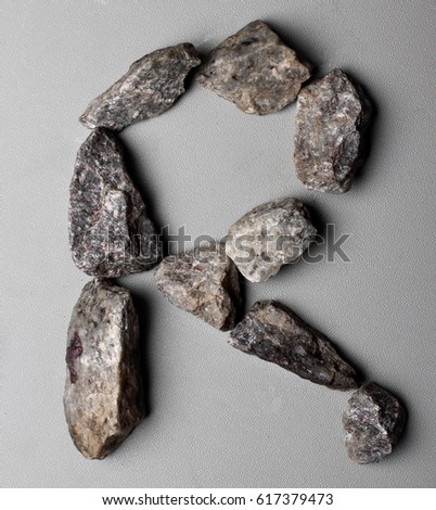 English letter R made of gray stones (gravel) on gray background. Uppercase letter.Stone alphabet