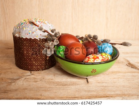 colored Easter eggs in green bowl, willow and Easter kulich cake on vintage wooden table