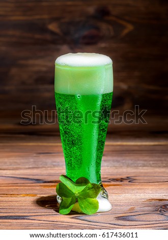 glass of green spilled foam beer on vintage wooden background, St Patricks day with leaf clover, close up