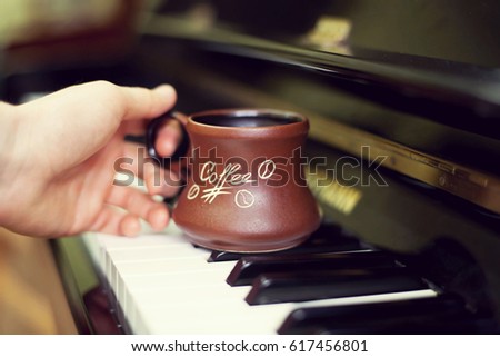 Cup of coffee on an old piano keyboard while composing. Evening time and some sun rays. Coffee mug on the piano keyboard