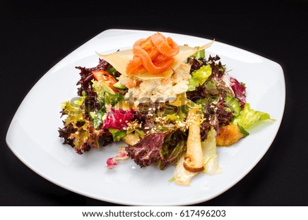 warm salad of fish, vegetables on a white plate, black background